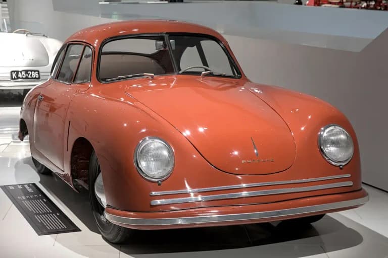 Salmon-colored early Porsche 356 coupe front three-quarter view in a museum