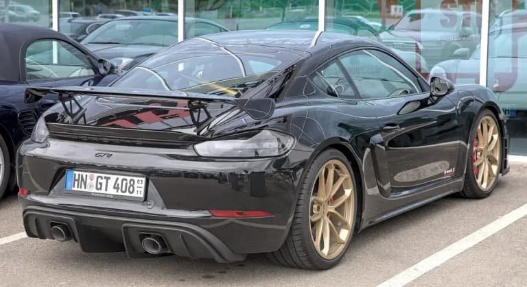 Black Porsche 718 Cayman GT4 rear view with fixed rear wing and gold wheels