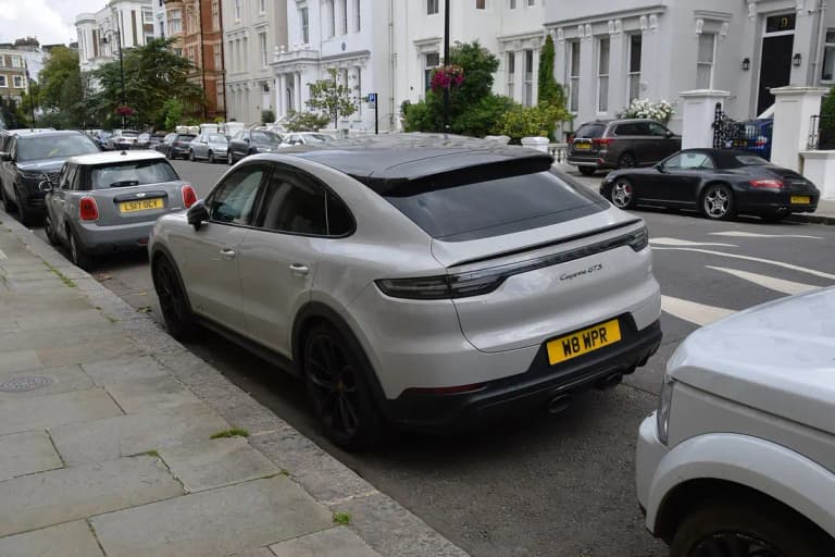 Chalk gray Porsche Cayenne GTS Coupe with black roof, parked on a residential street