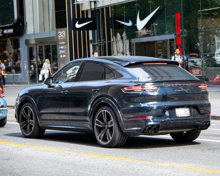 Dark blue Porsche Cayenne GTS Coupe, rear three-quarter view on a city street