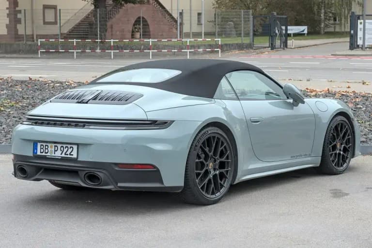 Gray Porsche convertible, a 992 911 Carrera Cabriolet, seen from the rear three-quarter with its soft top raised