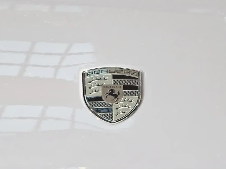 Close-up of the Porsche crest badge on the hood of a white Macan EV