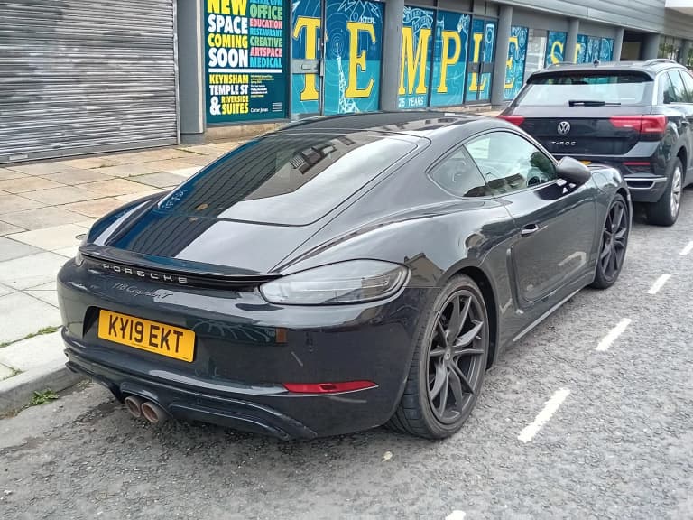 Black Porsche 718 Cayman T parked on a street, rear three-quarter view