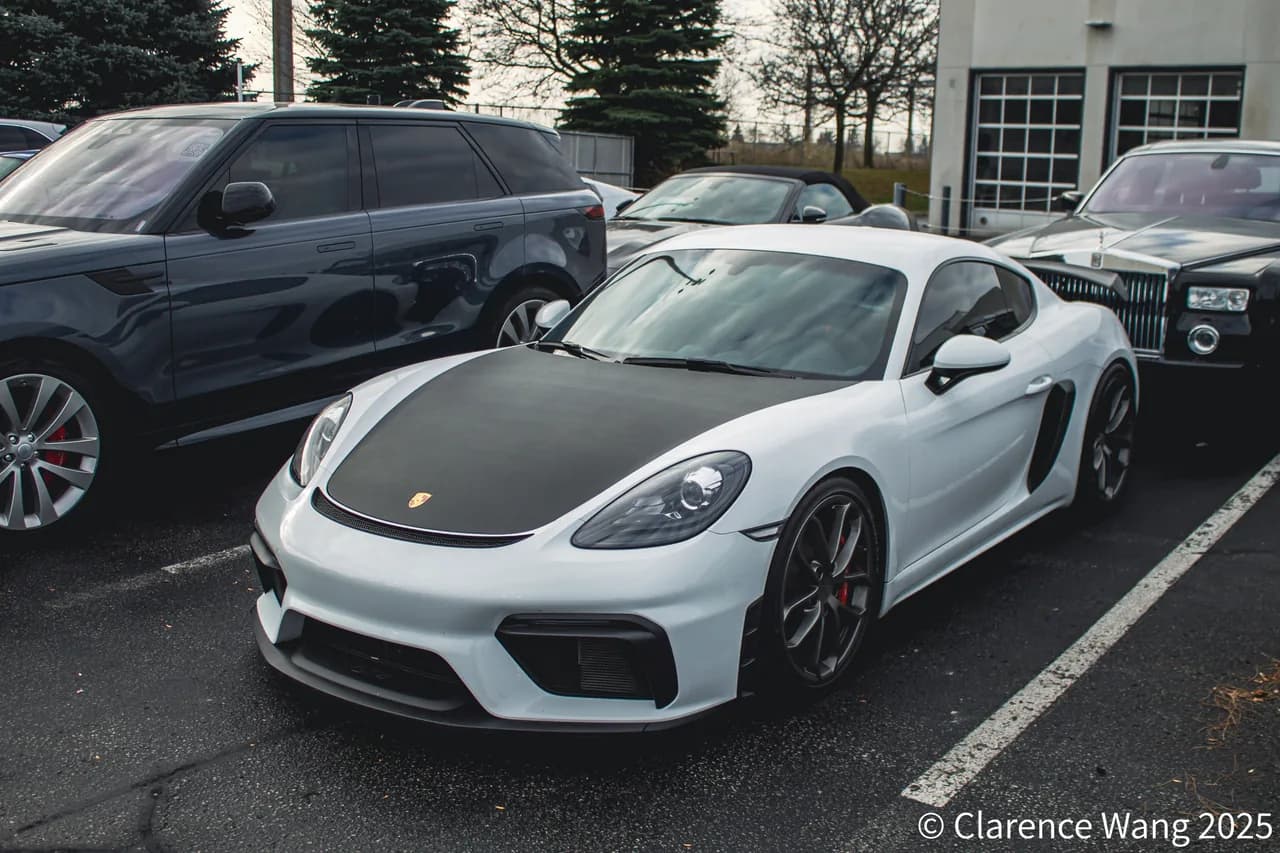 White Porsche 718 Cayman GT4 RS viewed from the front-left in a parking area.