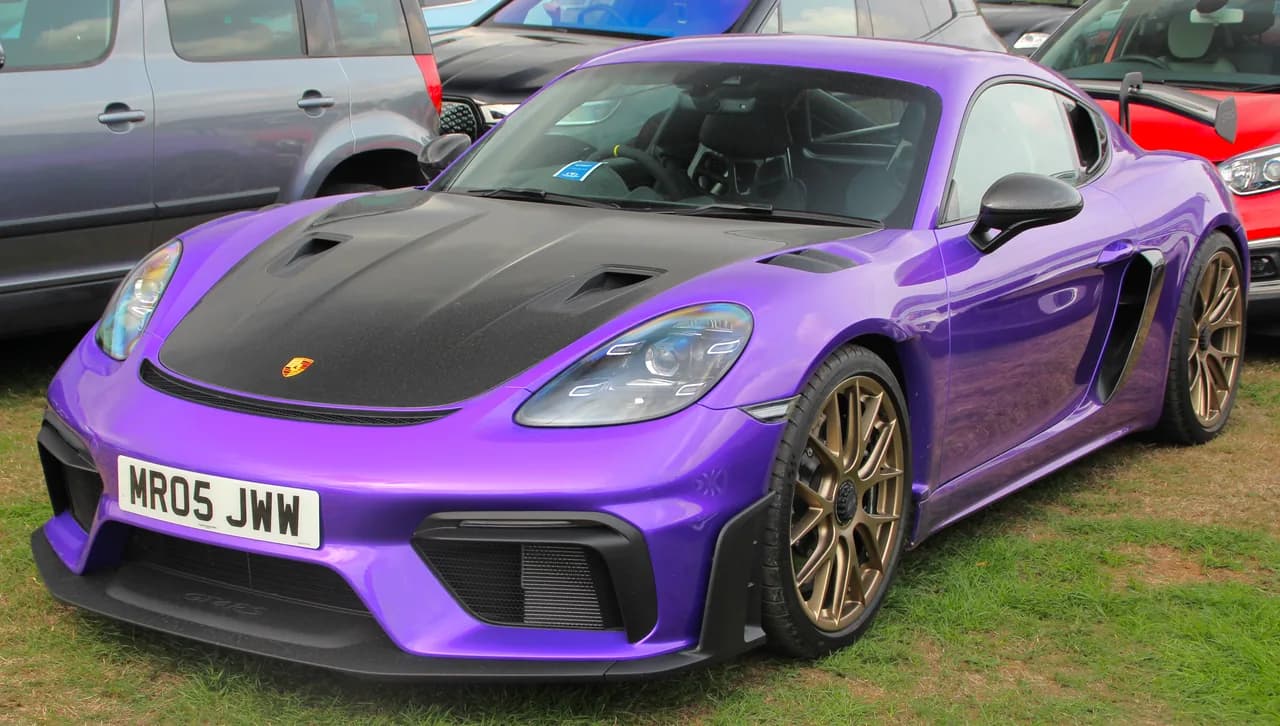 Purple Porsche 718 Cayman GT4 RS Weissach with exposed-carbon hood and bronze wheels, viewed from the front-left.