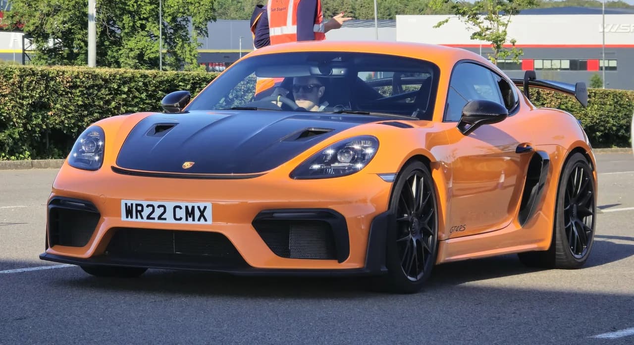 Orange Porsche 718 Cayman GT4 RS driving at a car event, showing its front aero and side intake.