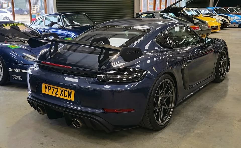 Dark blue Porsche 718 Cayman GT4 RS viewed from the rear-left, showing its fixed wing, diffuser, and twin exhaust outlets.