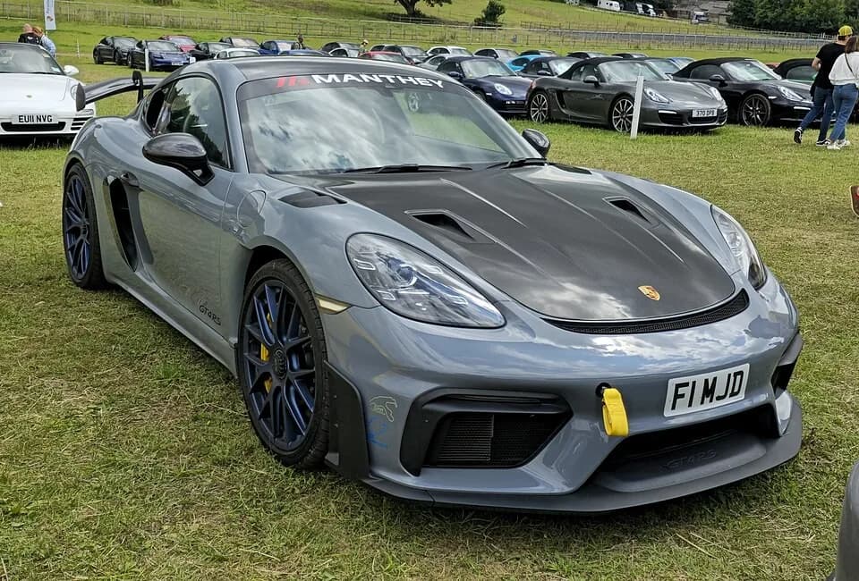Gray Porsche 718 Cayman GT4 RS viewed from the front-left, showing its door-side intake, vented hood, and rear wing.