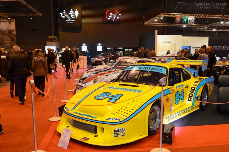 Yellow Porsche 934 number 84 race car shown from the front at Rétromobile