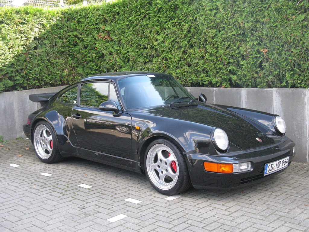 Porsche 911 964 Turbo parked on street, showcasing wide fenders and classic 1990s styling