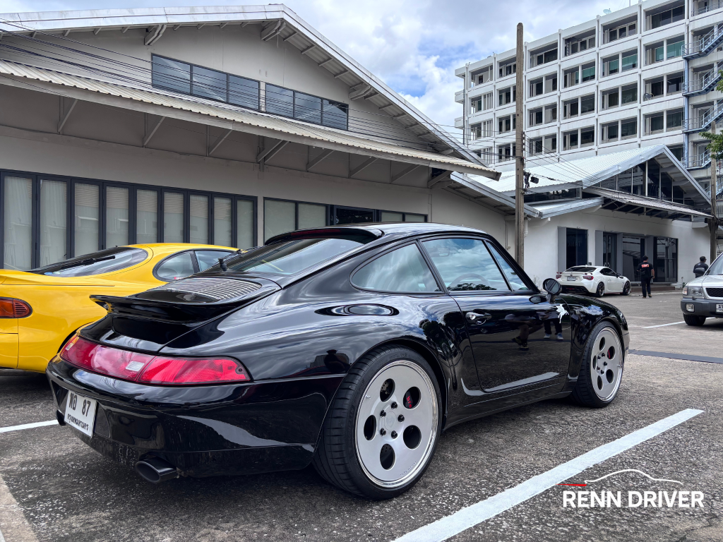 Black 993 Carrera with ducktail and dish wheels, rear three-quarter view.