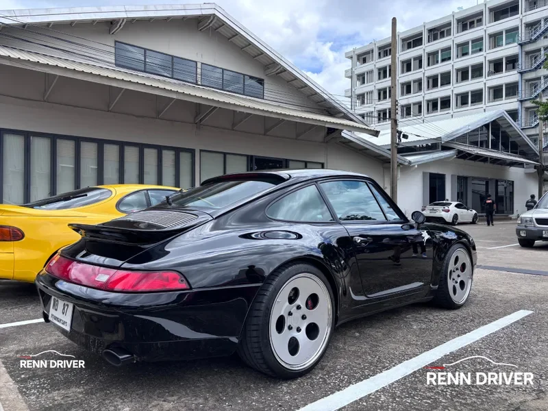Black 993 Carrera with ducktail and dish wheels, rear three-quarter view.