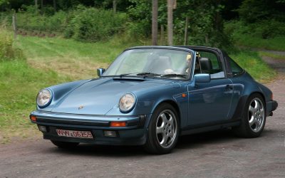 Blue Porsche 911 targa top with a forest behind it