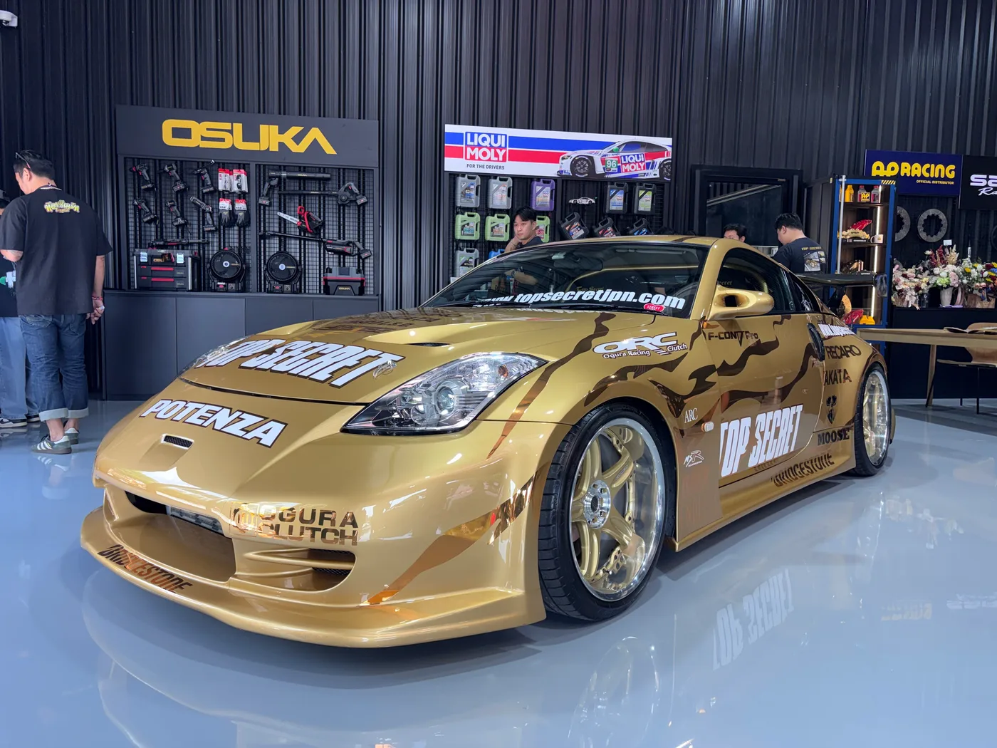 Gold Top Secret Nissan 350Z on display in front of Osuka and AP Racing brand walls